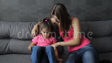 有孩子的女人用平板电脑坐在沙发上。 母亲带着孩子坐在沙发上用平板电脑